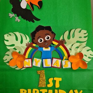 May include: Green gift bag with a rainbow, a cartoon character, and the words "NYLA'S 1ST BIRTHDAY" in yellow letters.