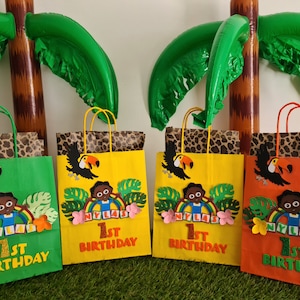 May include: Four green, yellow, and orange paper gift bags with jungle animal themes. Each bag has a toucan, a brown-skinned child, and the text "1st Birthday" and "NYLAS".