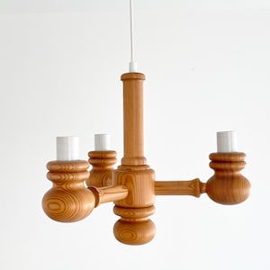 Puede incluir: Un candelabro de madera con cuatro portalámparas. La lámpara está hecha de madera de color claro y tiene una columna central con brazos que se extienden para sostener los portalámparas. Los portalámparas son blancos.
