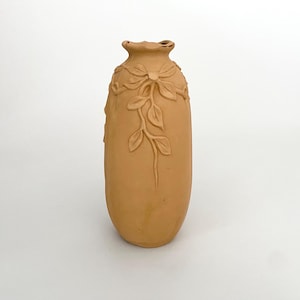 Może przedstawiać: Jasnobrązowy ceramiczny wazon z kwiatowym wzorem. Wazon ma zaokrąglone ciało i wąską szyjkę.