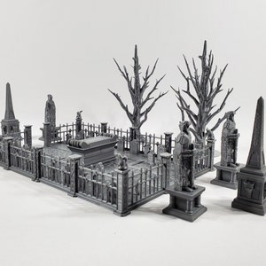 May include: A miniature gray cemetery scene with a gated enclosure, statues, a coffin, and leafless trees. The scene includes an obelisk and various gravestones, all in a detailed, gothic style. Ideal for tabletop gaming or model displays.