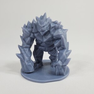 May include: A gray, 3D printed miniature of a stone golem, a mythical creature from fantasy games and stories. The golem is standing on a round base and has a spiky, rocky exterior.
