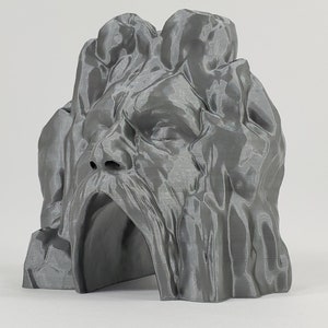 May include: A 3D printed gray stone sculpture of a face with a cave-like opening in the mouth.