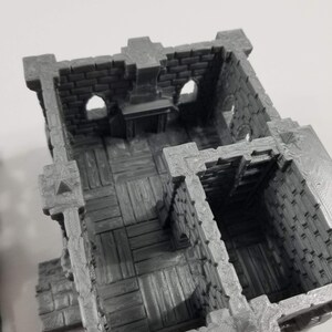 May include: A gray 3D printed miniature castle interior with a brick wall, a fireplace, and a wooden floor. The interior has two rooms, one with a wooden floor and the other with a brick wall.