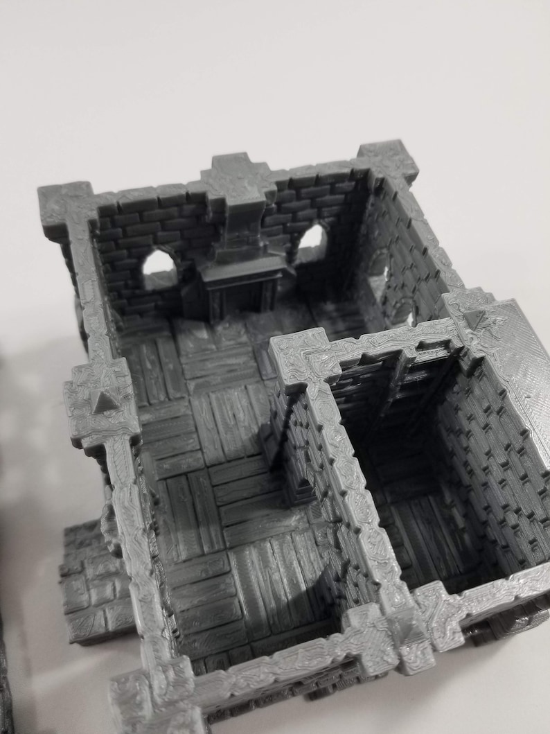 May include: A gray 3D printed miniature castle interior with a brick wall, a fireplace, and a wooden floor. The interior has two rooms, one with a wooden floor and the other with a brick wall.