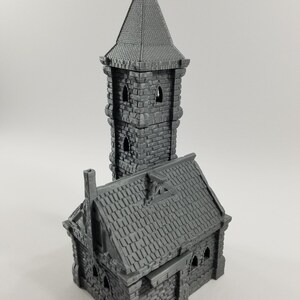 May include: A gray 3D printed miniature building with a tower and a smaller building attached. The tower has a pointed roof and windows. The smaller building has a gabled roof and a chimney.