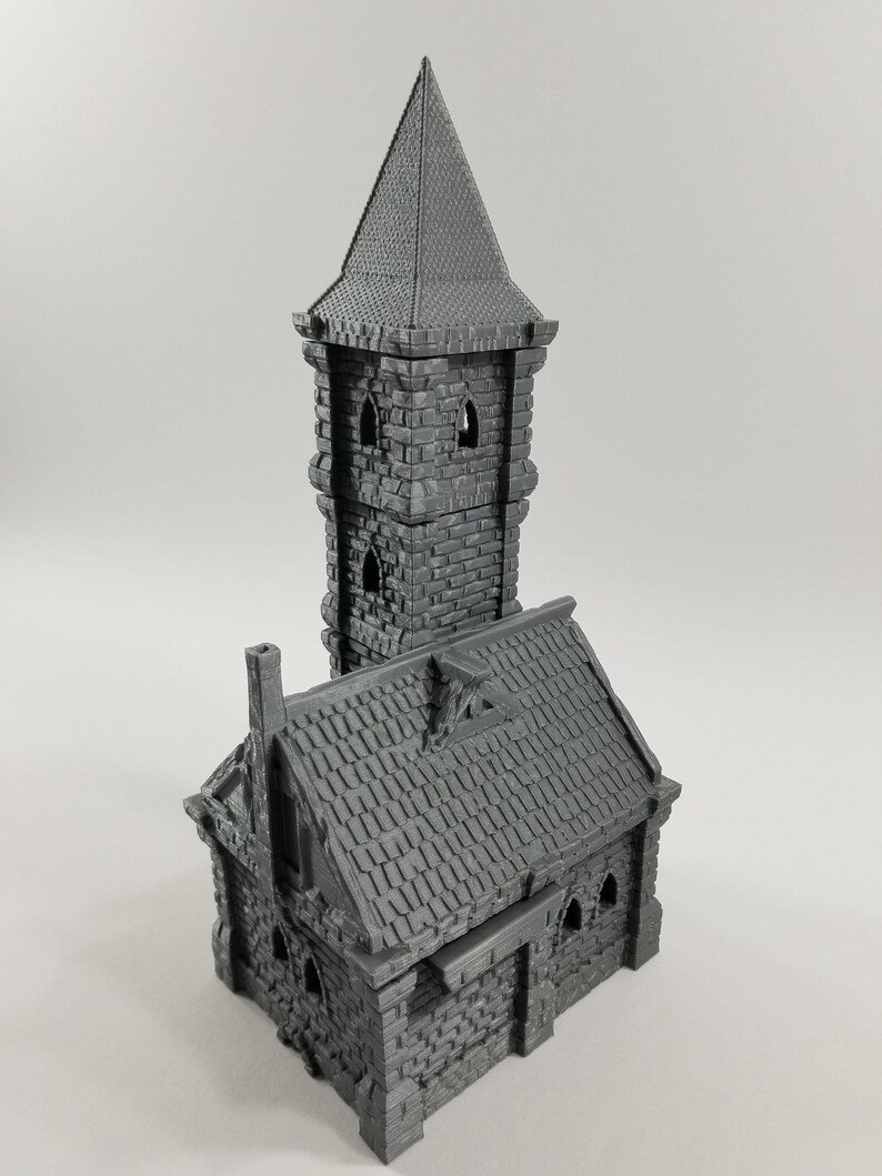 May include: A gray 3D printed miniature building with a tower and a smaller building attached. The tower has a pointed roof and windows. The smaller building has a gabled roof and a chimney.