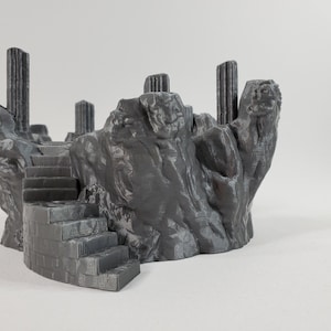 Può includere: Una rovina di pietra grigia stampata in 3D con una serie di scale che conducono a una piattaforma. La rovina ha diverse colonne ed è progettata per i giochi da tavolo.