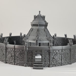 Puede incluir: Un modelo 3D impreso en gris de una estructura circular de piedra con un techo abovedado y una entrada decorativa. La estructura está rodeada por un muro con tallas decorativas.