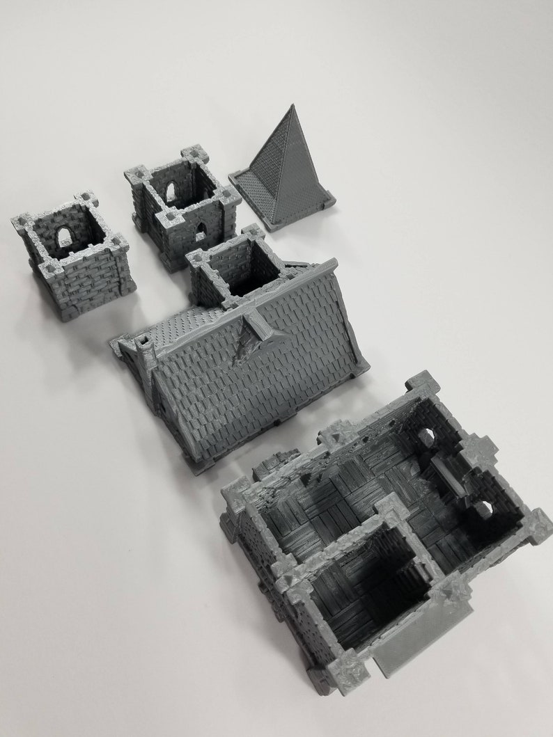 May include: A set of five gray 3D printed miniature building pieces. The pieces include a roof, a wall, a tower, and two smaller towers. The pieces are designed to be assembled into a small building.