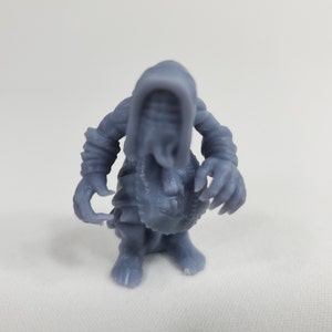 May include: A gray 3D printed miniature figure of a creature with a hooded head and clawed hands.