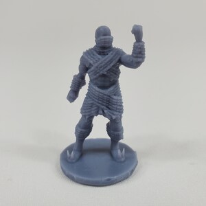 May include: A gray 3D printed miniature figure of a warrior wearing a woven armor and a skirt. The figure is standing on a round base.