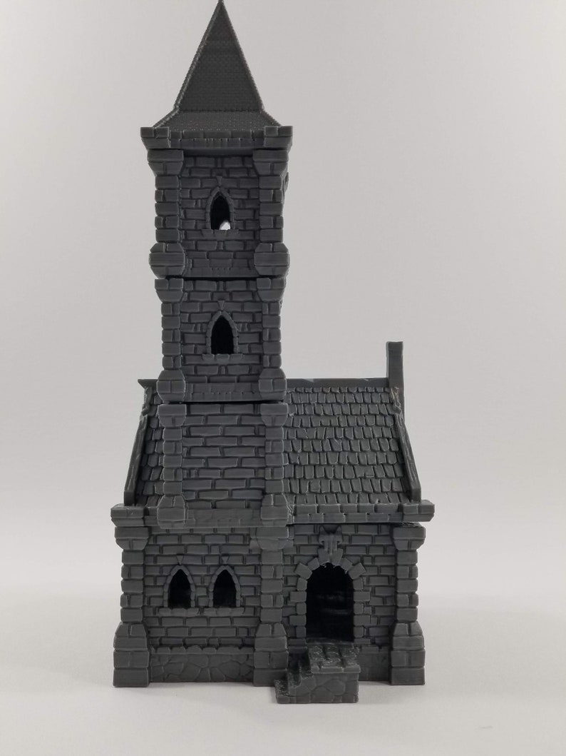May include: A gray 3D printed miniature of a stone church with a tall tower and a small entrance. The church has a pointed roof and several windows.