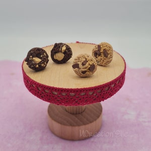 Peut inclure: Quatre mini-cookies aux pépites de chocolat sur un support en bois avec une bordure en dentelle rouge. Le support est sur une surface rose. MCreation'Elle est écrit sur la base du support.