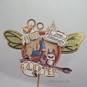 May include: A gold glitter cake topper with a Harry Potter theme. The topper features a circular design with a castle, owl, and broomstick. Text includes "10 ans", "Joyeux Anniversaire", and "Gabriel".