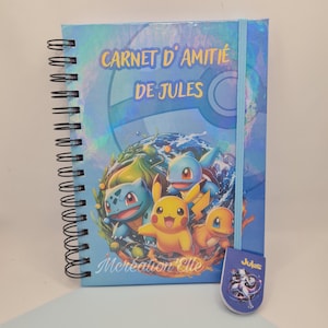 May include: Spiral-bound notebook with a blue cover featuring cartoon characters and the text "CARNET D'AMITIÉ DE JULES". A matching bookmark is attached. The notebook has a blue elastic band closure.