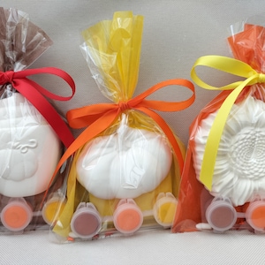 May include: Three clear plastic bags with orange, yellow, and brown ribbons tied around them. Each bag contains a white ceramic craft item, a pumpkin, a sunflower, and a turkey. Each bag also contains small containers of paint in various colours.