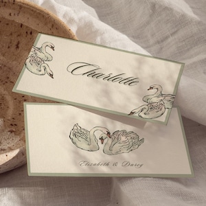 May include: A still life with a halved papaya and orange on a white cloth. A speckled ceramic bowl and two place cards with swan illustrations and names are in the foreground. The name "Charlotte" is visible on one card.