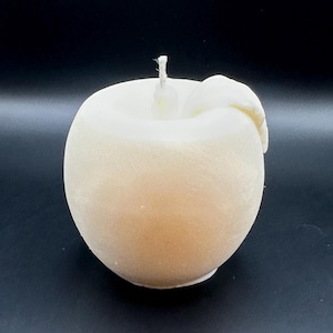 Peut inclure: Une bougie en forme de pomme de couleur cr&egrave;me, avec une m&egrave;che blanche et un d&eacute;tail en forme de feuille. La bougie a une forme lisse et arrondie, sur fond sombre. Cette bougie d&eacute;corative est con&ccedil;ue pour ressembler &agrave; une pomme fra&icirc;che.