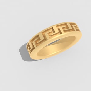 Può includere: Un anello color oro con un motivo a chiave greca attorno alla fascia. L'anello è di colore pieno e poggia su una superficie bianca. Il design dell'anello è un motivo geometrico ripetitivo.