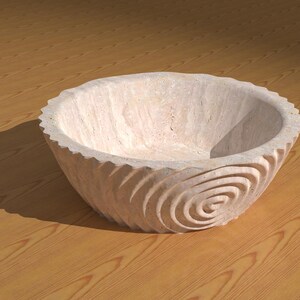 May include: A white stone bowl with a spiral design carved into the exterior. The bowl is sitting on a wooden surface.