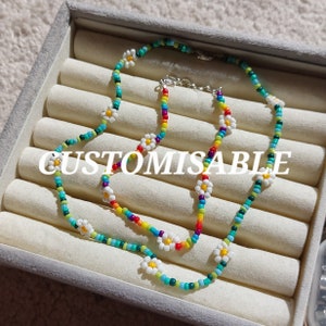 Può includere: Una collana di perline colorate con accenti di fiori di margherita bianchi. La collana è a strati e ha un design personalizzabile.