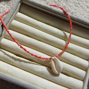 May include: A pink, orange and gold beaded necklace with a white seashell pendant.