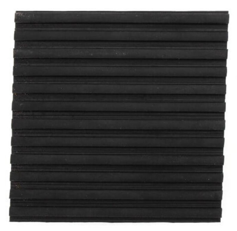 May include: A square, black rubber mat with a ridged surface. The ridges run horizontally across the mat, creating a textured pattern. The mat appears to be made of a durable material.