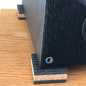 May include: Black speaker with cork and rubber isolation pads on a wooden surface.