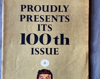 Puede incluir: Una edición vintage de la revista MAD, número 100 de enero de 1966. La portada presenta el logotipo rosa de la revista, el texto «PROUDLY PRESENTS ITS 100th ISSUE» y una ilustración de dibujos animados de Alfred E. Neuman con un bocadillo que dice «Big deal!».