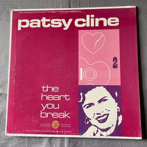 May include: A vintage vinyl record album cover for Patsy Cline, featuring a magenta background with white text. The album title is "The Heart You Break." The cover includes a graphic of a heart with a lightning bolt and a guitar.