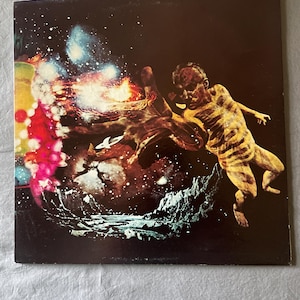May include: Album cover art featuring a cosmic scene with a figure reaching towards a colorful nebula. The artwork has a dark background with a mix of reds, yellows, and blues, and a figure in the foreground.