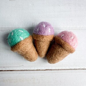 Könnte beinhalten: Drei Filz-Eiswaffeln in verschiedenen Farben: grün, lila und rosa. Jede Waffel hat weiße Streusel.