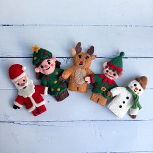 May include: A collection of handmade felt Christmas ornaments. The set includes Santa Claus, an elf, a reindeer, a snowman, and another elf. Each ornament is brightly colored and detailed, perfect for holiday decorating.