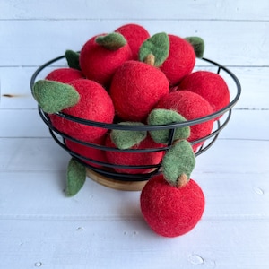 May include: A black wire basket filled with red felt balls that resemble apples, each with a green felt leaf attached.