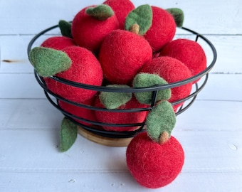 Puede incluir: Una cesta de alambre negra llena de bolas de fieltro rojo que se asemejan a manzanas, cada una con una hoja de fieltro verde.