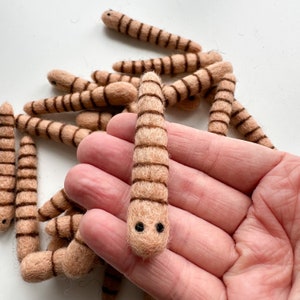 May include: A pile of brown felt worms with black eyes. The worms are about 2 inches long and have a striped pattern.
