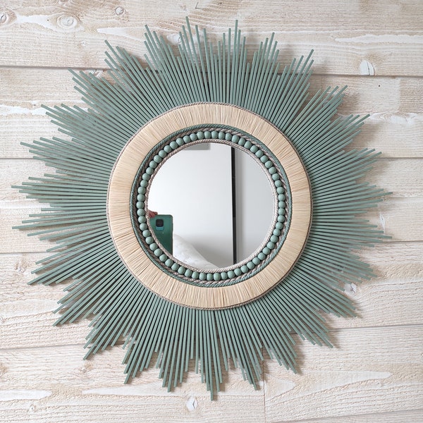 Miroir rond en bois teinté d'un vert tendance, il est cerné de cordes de lin et de colliers en perles de bois