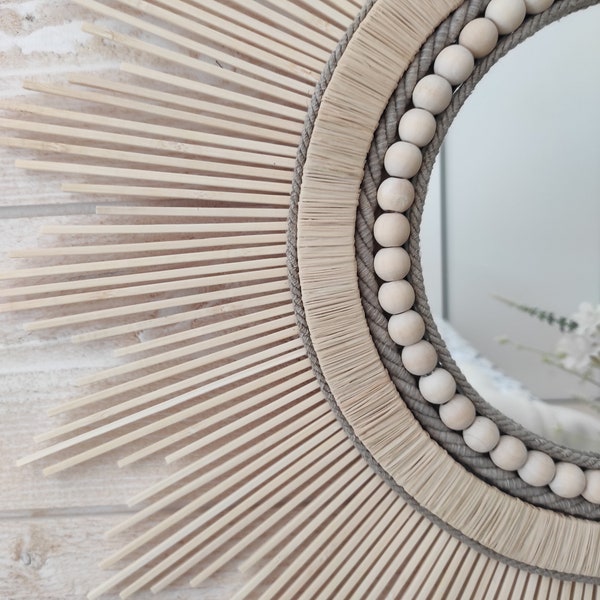 Ronde spiegel van natuurlijk hout omgeven door een gevlochten raffia-rand, linnen touwen en een parelsnoer