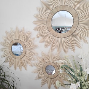Peut inclure: Trois miroirs ronds avec un design en forme de soleil, faits de bâtonnets de bois naturel. Les miroirs sont de tailles différentes et sont montés sur un mur blanc.