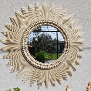 Grote ronde spiegel van natuurlijk raffia, omlijst met linnen koorden en twee kralenkettingen van cederhout. Ju0256