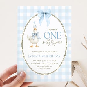 May include: A rectangular birthday invitation card featuring a light blue and white gingham pattern. The center displays an oval frame with a blue bow, a goose wearing a party hat and bow, and the text: JASON IS ONE SILLY GOOSE, PLEASE JOIN US TO CELEBRATE JASON'S 1ST BIRTHDAY, SATURDAY, JUNE 14TH, 3 PM, 4239 DIANE STREET, ATASCADERO, RSVP TO OLIVIA AT 123-456-7890.
