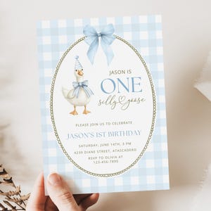 May include: A rectangular birthday invitation card featuring a light blue and white gingham pattern. The center displays an oval frame with a gold border, a light blue bow, and a white goose wearing a party hat and blue bow. Text reads: JASON IS ONE silly goose, PLEASE JOIN US TO CELEBRATE JASON'S 1ST BIRTHDAY, SATURDAY, JUNE 14TH, 3 PM, 4239 DIANE STREET, ATASCADERO, RSVP TO OLIVIA AT 123-456-7890.