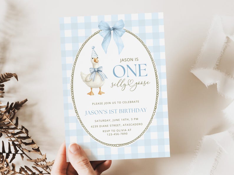 May include: A rectangular birthday invitation card featuring a light blue and white gingham pattern. The center displays an oval frame with a gold border, a light blue bow, and a white goose wearing a party hat and blue bow. Text reads: JASON IS ONE silly goose, PLEASE JOIN US TO CELEBRATE JASON'S 1ST BIRTHDAY, SATURDAY, JUNE 14TH, 3 PM, 4239 DIANE STREET, ATASCADERO, RSVP TO OLIVIA AT 123-456-7890.