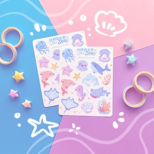 Puede incluir: Dos hojas de pegatinas con el tema "Bajo el Mar", con ilustraciones de vida marina como delfines, medusas e hipocampos. Las pegatinas son de colores pastel, con elementos decorativos como cinta adhesiva washi y estrellas de origami.