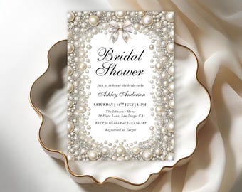 Puede incluir: Una invitación a una despedida de soltera con un diseño de perlas y lazo. La invitación incluye el texto "Bridal Shower" y los detalles del evento, incluido el nombre de la novia, la fecha, la hora y el lugar. La invitación está colocada sobre un plato blanco decorativo.