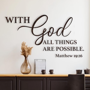 Op de afbeelding: Keukeninterieur met donkerbruine kasten, een houten vloer en een zwarte stoel. De muur toont de quote "WITH God ALL THINGS ARE POSSIBLE. Matthew 19:26" in donkerbruine letters. Een vaas met gedroogde bloemen staat op het aanrecht.