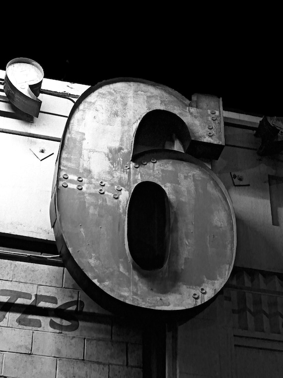 Rusting metal sign six 6 at night.