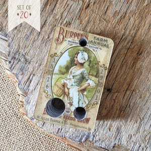 May include: A rectangular tag featuring a vintage Burpee's Farm Annual illustration of a person holding a basket in a field. The tag has three circular holes and text including 1876, 1901, and W. Atlee Burpee & Co. Philadelphia. A banner reads Set of 20.