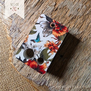 May include: A rectangular display card with three circular holes, featuring a white background printed with a colorful floral pattern of red, orange, and grey flowers, green leaves, and a small blue hummingbird. The text SET OF 20 is visible.